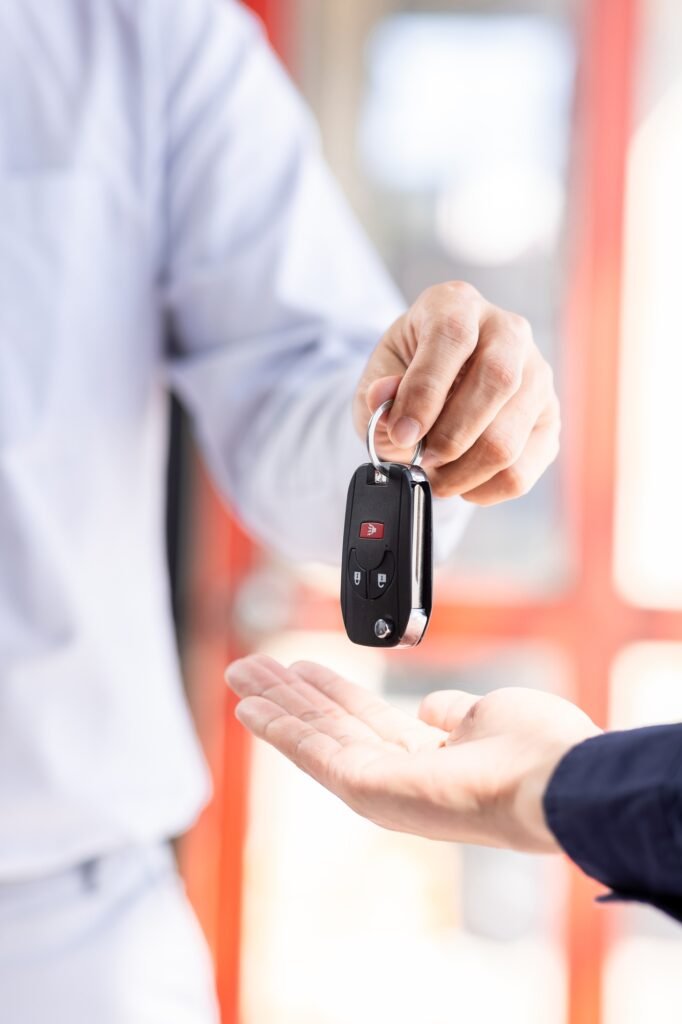 Dealer salesman giving car key to owner. client signing insurance document or rental car lease form